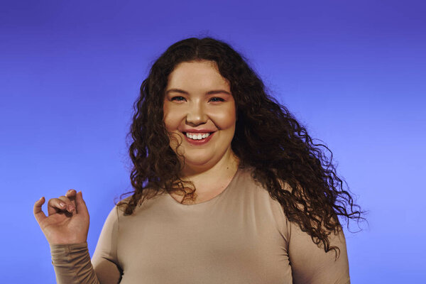 A beautiful plus size woman exudes confidence while playfully posing in front of a vivid backdrop.