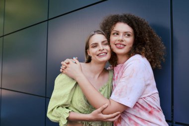 Two young women embrace warmly, celebrating their bond in a vibrant outdoor setting. clipart