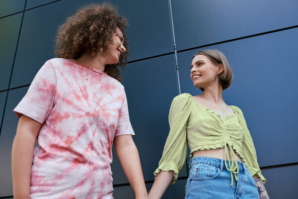 Две молодые женщины, улыбаясь и соединяясь, разделяют нежный момент на открытом воздухе.