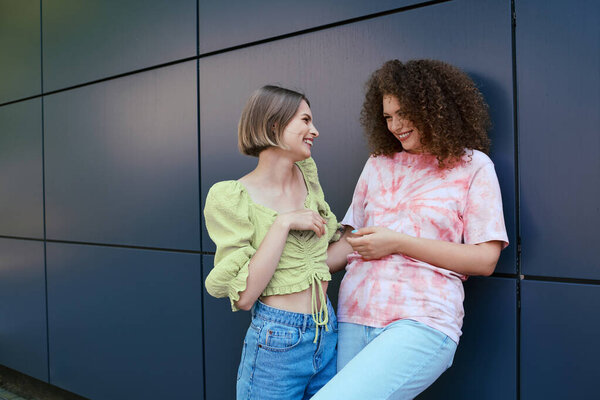 Две молодые женщины тепло взаимодействуют друг с другом, излучая счастье в оживленном окружении.