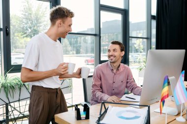 A stylish gay couple enjoys a light hearted conversation over coffee in a modern office setting. clipart