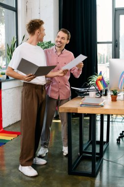 Two stylish men engage in a lively discussion amidst a bright, colorful workspace. clipart