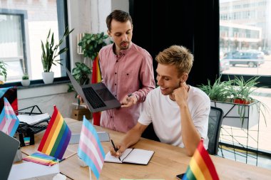 Two men share ideas in a vibrant office filled with pride flags, fostering a creative atmosphere. clipart