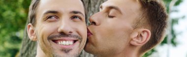 Two joyful men share an affectionate kiss surrounded by vibrant nature, radiating happiness. clipart