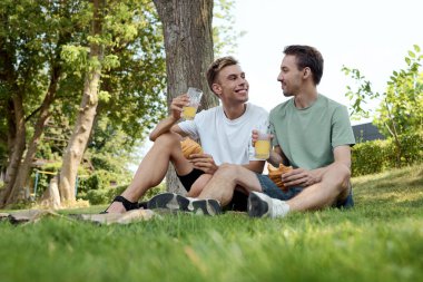 A dapper couple enjoys refreshing drinks and smiles while sitting on the grass. clipart