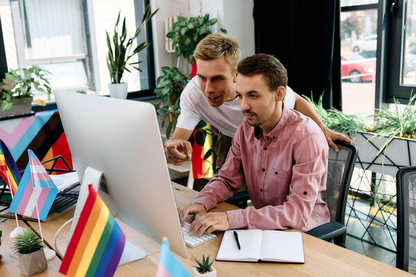 Двое мужчин с энтузиазмом работают за столом, украшенным яркими флагами на оживленном рабочем месте..