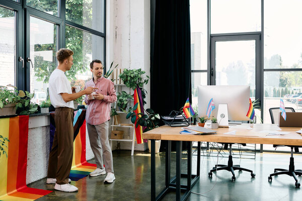 A joyful couple shares a moment in a lively office decorated for pride, surrounded by plants.