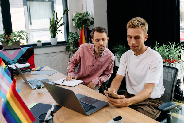 A handsome couple collaborates enthusiastically in a vibrant office adorned with pride flags.