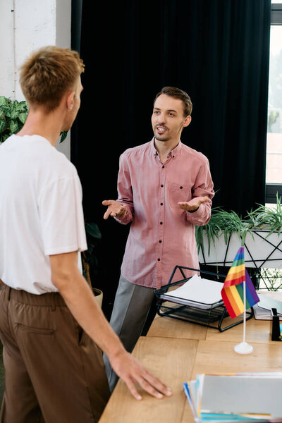 Двое молодых людей участвуют в оживленной дискуссии, делясь улыбками в стильной офисной обстановке.