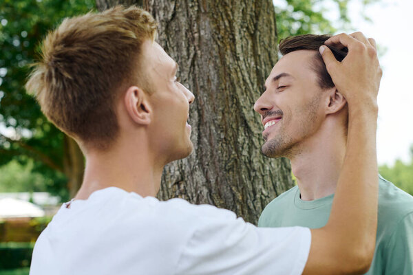 Два радостных мужчины обнимаются, разделяя искреннюю улыбку в яркой обстановке на открытом воздухе.