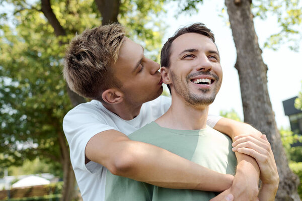 A couple shares a tender embrace, laughing together while enjoying a warm day in nature.