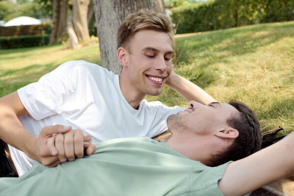 Two handsome partners share a tender moment while relaxing on the grass in a sunny park.