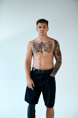 A tattooed young man stands proudly in a modern studio, showcasing his prosthetic leg and body art. clipart