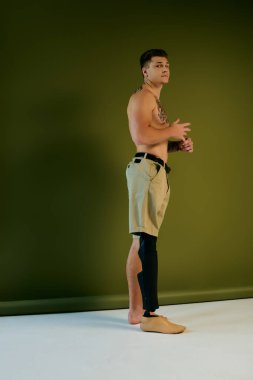 Dövmeli genç bir adam yaratıcı bir stüdyo ortamında poz verirken protez bacağını sergiliyor..