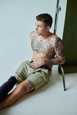 A tattooed man sits against a backdrop, showcasing his unique style and resilient spirit confidently. clipart