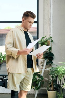 Protez bacaklı genç bir adam çağdaş, bitki dolu bir ofiste önemli belgeleri inceliyor..