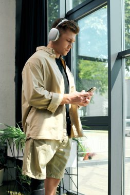 Protez bacaklı genç bir adam, parlak ve modern bir ofis yerinde dururken telefonuna odaklanıyor..