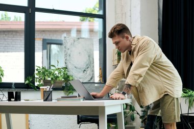 A handsome young man uses his laptop at a contemporary office desk, showcasing determination and focus. clipart