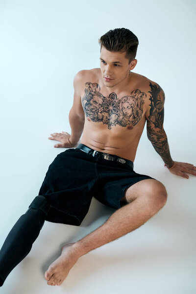 Татуированный молодой человек, демонстрирующий свои поразительные дизайны и силу, сидя в яркой студии.