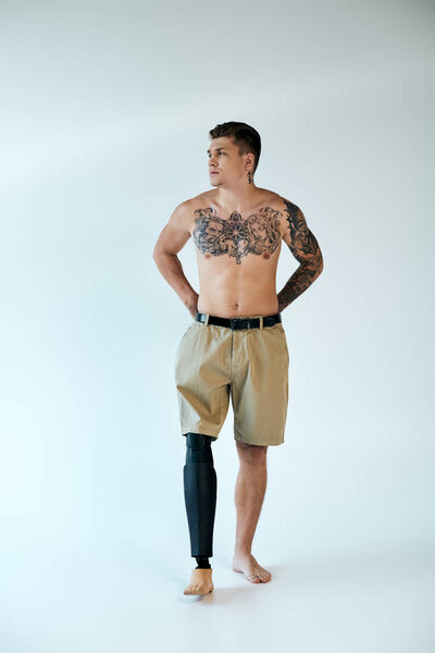 Молодой человек со сложными татуировками уверенно позирует в студии, демонстрируя свою протезную ногу и силу.