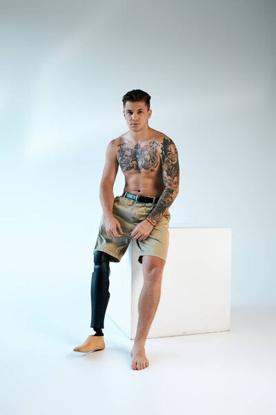Татуированный молодой человек демонстрирует свою протезную ногу, позируя в стильной студии.