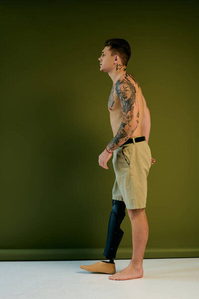 Татуированный молодой человек изящно ходит на протезной ноге, демонстрируя силу и стойкость в спокойной студии..