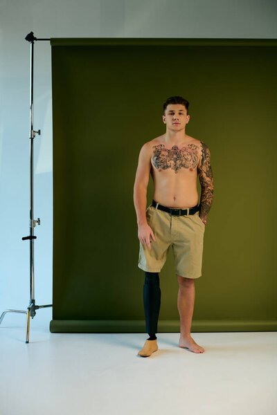 Молодой человек со сложными татуировками уверенно стоит в студии, подчеркивая свою протезную ногу..