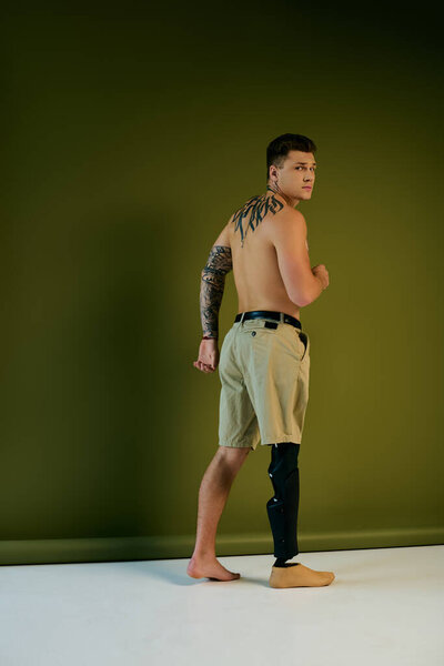 Молодой человек с яркими татуировками стоит с гордостью, демонстрируя свою протезную ногу в творческой студии.