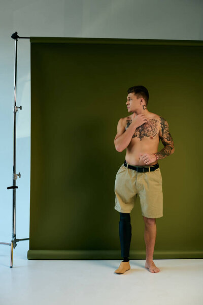 Татуированный молодой человек стоит с протезной ногой, демонстрируя свое тело в творческой студии.