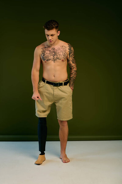 Татуированный молодой человек уверенно стоит в студии, подчеркивая свою протезную ногу и уникальный стиль.