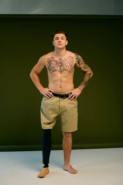 Татуированный молодой человек уверенно позирует в студии, подчеркивая свою протезную ногу и художественные татуировки.