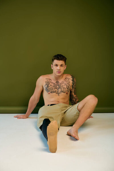 Татуированный молодой человек сидит в студии, его протезная нога видна, отражает силу и стойкость.