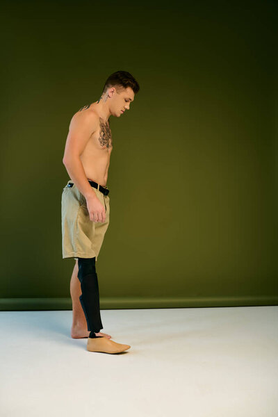 В творческой студии молодой человек с татуировками спокойно стоит, демонстрируя свою протезную ногу и стильные шорты..