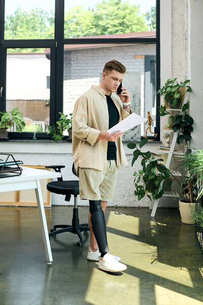 Самоотверженный молодой человек с протезной ногой разговаривает по телефону, стоя в вдохновляющем рабочем пространстве.