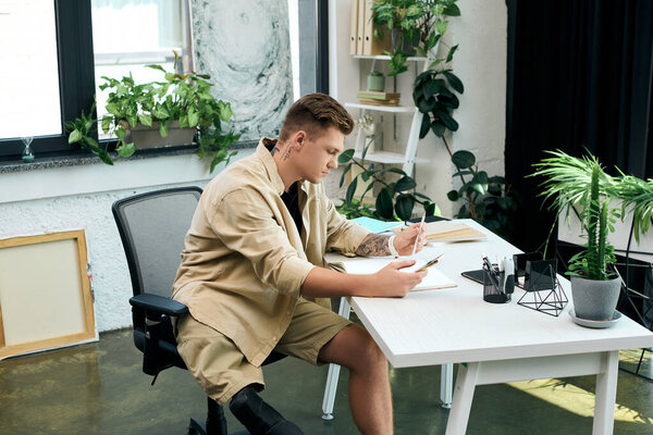 Молодой человек с протезной ногой сосредоточен на своей работе за стильным офисным столом в окружении зелени.