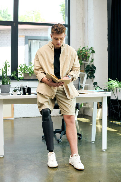 Молодой человек с протезной ногой сосредоточен на чтении книги в стильной современной офисной обстановке.
