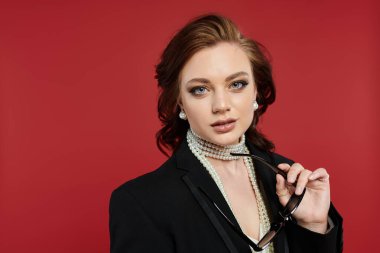 Zarif giyinmiş genç bir kadın çarpıcı bir arka plana karşı güvenle duruyor..