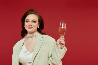 Şık bir genç kadın neşeyle kutlama yapar, parlak bir gülümsemeyle, ışıl ışıl bir içecek tutar..