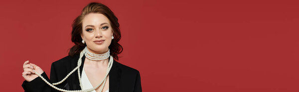 With a confident smile, a young woman elegantly draped in pearls stands out against a bold backdrop.