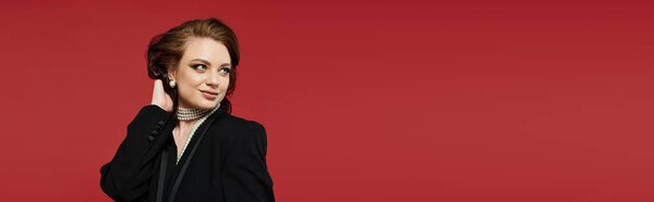 A young woman dressed elegantly showcases her style and confidence against a bold red backdrop.