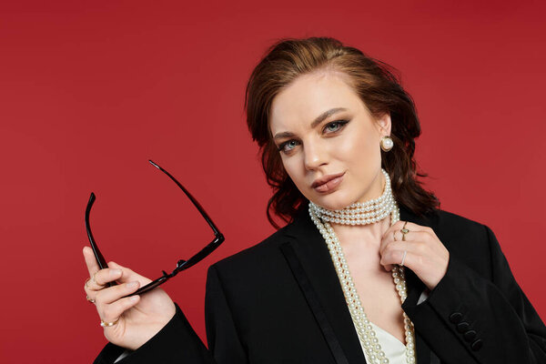 A beautiful woman exudes elegance while holding stylish glasses, dressed in formal attire.