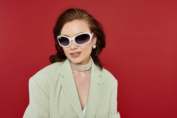 Молодая женщина, элегантно одетая в стильные солнцезащитные очки и жемчужные аксессуары, излучает уверенность.