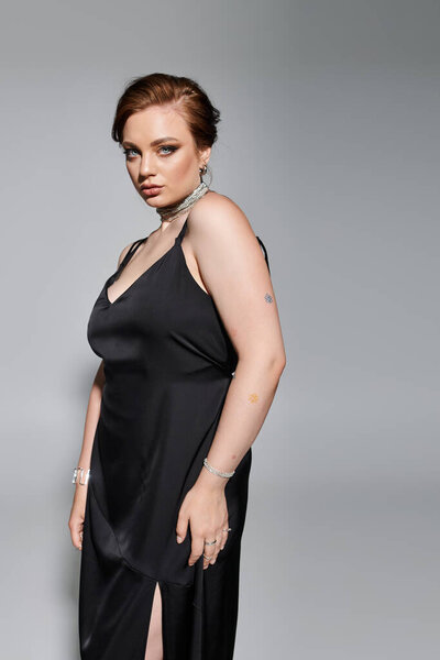 Молодая женщина в элегантном черном платье элегантно позирует, демонстрируя свой стиль и уверенность.