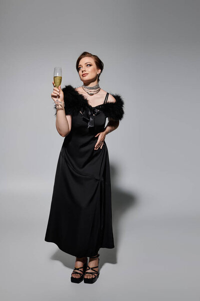 A stylish young woman toasts with a champagne glass while wearing a stunning black dress.