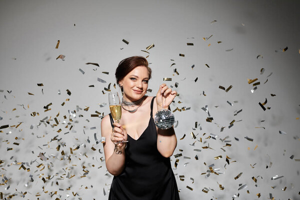 The young woman raises a glass of champagne, smiling amid a flurry of sparkling confetti.