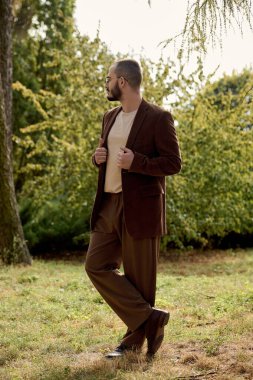 Şık sonbahar kıyafetleri giymiş yakışıklı bir adam canlı sonbahar yeşillikleri arasında rahatça poz verir..