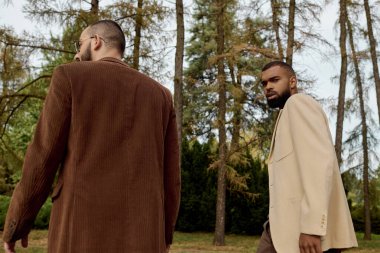 Şık sonbahar kıyafetleri giymiş iki yakışıklı adam manzaralı bir alanda huzurlu bir anın tadını çıkarıyorlar..