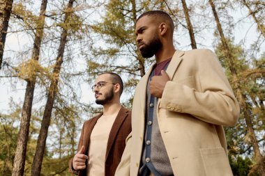 Two well-dressed men stroll through a vibrant autumn landscape, embracing the season's charm. clipart