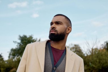 Şık bir adam, canlı sonbahar yaprakları arasında, kendine güveni tam bir şekilde duruyor, mevsimlik tarzını ve zarafetini sergiliyor..