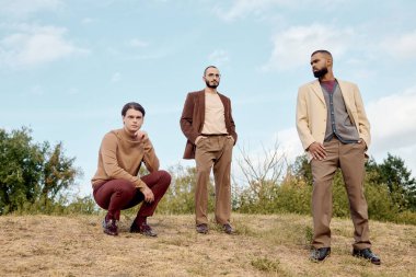 Handsome men dressed in autumn attire pose confidently in a peaceful field surrounded by nature. clipart